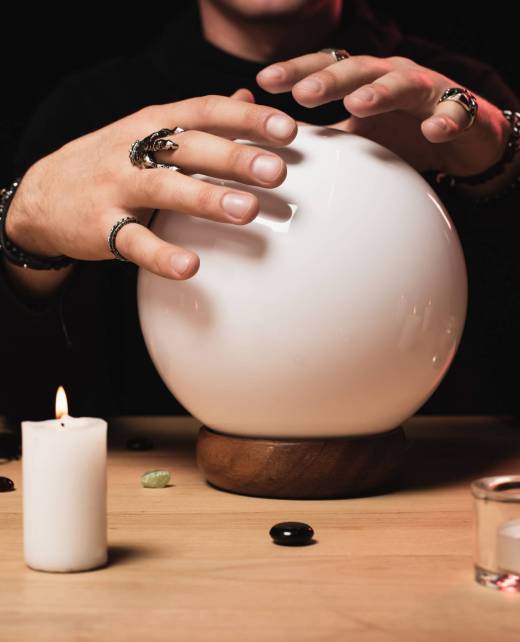 cropped view of esoteric holding hands above crystal ball near candles isolated on black